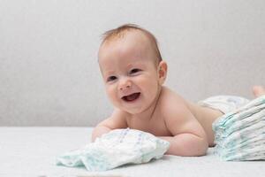 A little boy at the age of 5 months lies in a diaper on a white background and looks at the camera. Stack of diapers, anti-leak, soft and comfortable. Copy space for text photo