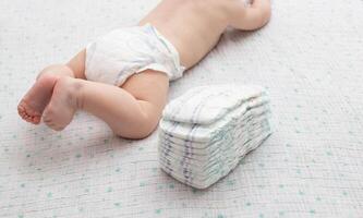 The legs of a baby in a diaper against the background of a stack of children's comfortable diapers, close-up. Copy space for text photo