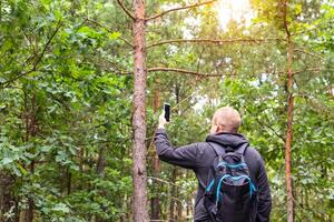 A man holds a smartphone in his hand on the background of the forest. The concept of poor cellular reception in the forest. Define locations. Copy space for text photo