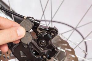 new brake pads in hand on the background of a bicycle brake caliper. Replacement of brake pads, close-up photo