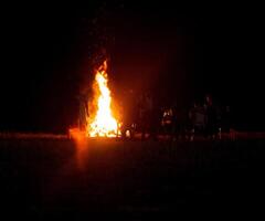 People relax on a holiday in the forest near a large bonfire at night. National holiday background, copy space photo