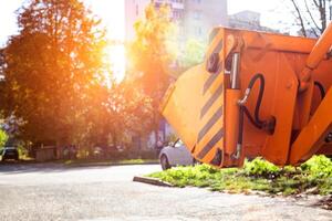 Yellow bucket of a tractor excavator on the background of houses in the city in autumn. Residential building concept, industry, copy space for text photo