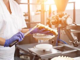 The pastry chef makes cake using modern equipment for the production of cakes. Line for spreading cream on cake, biscuit photo