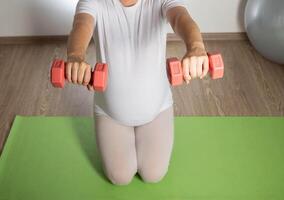 A pregnant girl goes in for sports in the 3rd trimester of pregnancy. Fitness and Pilates. Women's health. Exercises with dumbbells. photo
