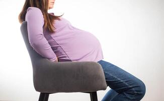 Pregnant girl sits on a chair at the workplace, white background. The concept of maternity leave and working conditions under the law. Benefits and maternity leave. Copy space for text photo