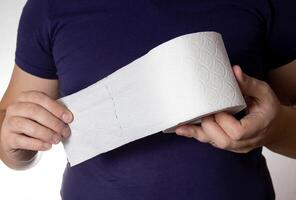 A man holds a roll of toilet paper in his hands against the background of a blue T-shirt. Concept paper for dry closets and digestive problems, close-up photo