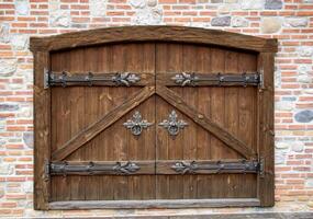 Semicircular wooden gate with wrought iron doorknobs in a brick building. Ancient architecture, close-up photo