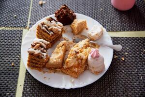 Leftovers in a plate on the table with sweets cakes, close-up photo