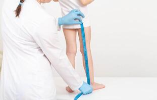 A doctor in blue gloves with a measuring tape measures the length of the legs of a 4-year-old caucasian girl. Child development and growth concept. Copy space for text photo