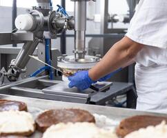 The pastry chef makes cake using modern equipment for the production of cakes. Line for spreading cream on biscuit cake. Industry photo