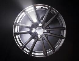 Modern beautiful car alloy wheel in the form of rays that is highlighted by rays of light and sparkle, black background photo