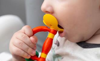 A child holds a rubber toy massager for teething in his hand. Itching and salivation from the mouth. First teeth. Help with teething, close-up photo