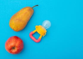 Fruits on a blue background next to a children's nibbler, close-up. Cognitive nutrition with vitamins and the development of the chewing reflex in children, close-up photo