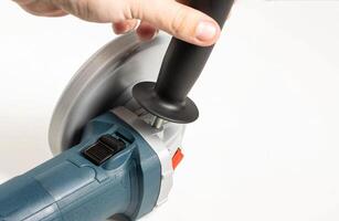 The hand twists the extra handle into the angle grinder for a comfortable grip. Copy space for text photo