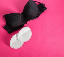 Black bra with liners for the female breast against the flow of milk on a pink background. Womens breast pads, lactation. Copy space for text photo