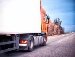An orange truck is transporting goods in a refrigerated trailer on a motorway. Logistics and industry concept in cargo transportation, driver forwarder, copy space photo