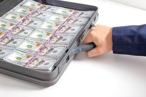 The hand of a man businessman holds a modern briefcase with money dollars on a white background. Fraud and confiscation concept, money agent photo