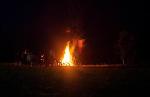 People relax on a holiday in the forest near a large bonfire at night. National holiday background, copy space photo