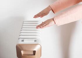 Children's hands on the background of an oil electric heater on a white background. Concept for turning on heating in apartments, temperature in the house. photo