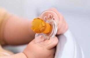 A torn and chewed silicone nipple in the hands of a baby. The concept of problems with bite in children due to the pacifier. Teething, pediatrics photo