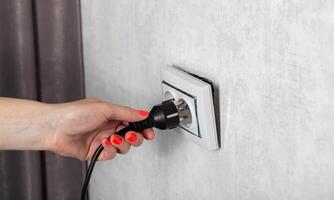 The girl removes the electrical plug from the socket and breaks the socket out of the socket. Incorrect removal of the electrical plug. Risk of electric shock, close-up photo