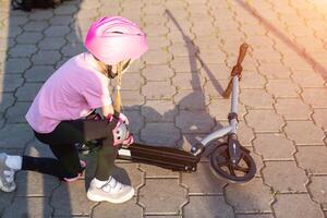 A 7-year-old girl in a pink helmet and protective gear fell off a scooter. The concept of safe riding a scooter and a bicycle without injury. Copy space for text photo