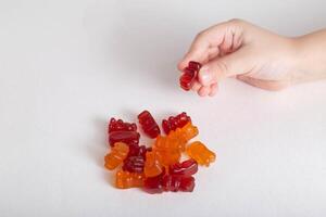 Small child's hand holds multicolored kids vitamins teddy bear on white background, isolate. Multivitamins photo