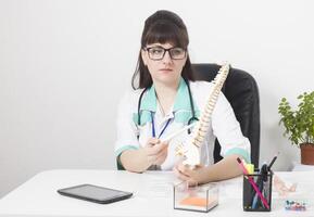 Doctor woman in a medical office with a mock up of the spine in her hands. Back pain treatment concept, doctor neurologist and vertebrologist, copy space for text photo