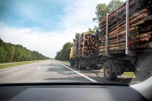 Transportation of forest logs on a truck trailer in summer on an asphalt road. Timber transportation, forest industry. Copy space for text photo