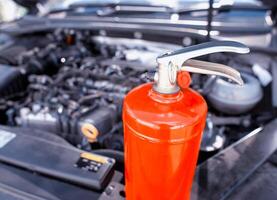 Car fire extinguisher on the background of the car engine. Extinguishing class of fire extinguisher, expiration date. Copy space for text photo