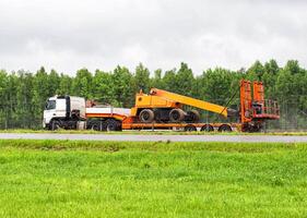 A truck with a trailer transports oversized cargo in the summer on the road against the backdrop of the forest. Transportation of oversized aerial platform photo