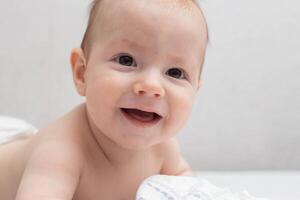A little boy at the age of 5 months lies in a diaper on a white background and looks at the camera. Stack of diapers, anti-leak, soft and comfortable. Copy space for text photo