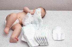 A little caucasian baby boy in a diaper lies on a white background and plays with a bunch of diapers. Copy space for text photo
