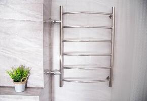 Modern chrome heated towel rail with warm water on a tiled wall. There is a flower on the shelf. Beautiful bathroom item. photo