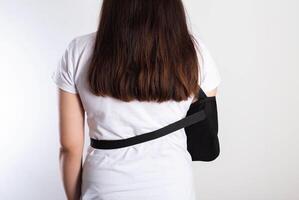 A girl on a white background with a black supporting medical bandage after a dislocation of the shoulder joint and a bone fracture. Rehabilitation after injury, orthopedics and traumatology photo