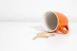 Spilled coffee from an orange cup on a white table in the office, copy space photo