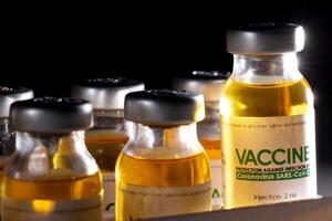 Vials with coronavirus vaccine in packaging on a black background and illuminated by a beam of light. Population vaccination recipe, vaccine research, SARS-Cov-2 photo