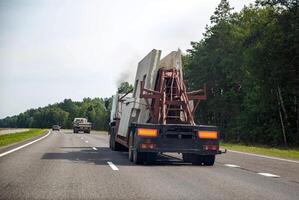 Semi-trailer truck tractor panel transporter transports reinforced concrete slabs for building a house. Transportation of spare parts for the house on the background of the forest on the highway. photo