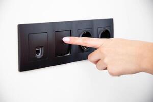 The girl presses the button of the broken electrical switch combined with the socket. Electric shock concept with faulty equipment, close-up photo
