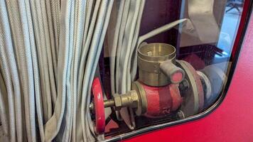 Firefighting equipment displayed in a fire station, showcasing a hose connection valve with white hoses coiled nearby, illuminated by overhead lighting during daylight hours photo