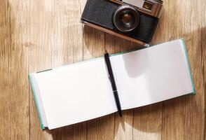 A retro film camera and a notepad with a pen lie on a wooden table, under the rays of the morning sun photo
