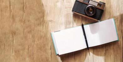 A retro film camera and a notepad with a pen lie on a wooden table, under the rays of the morning sun photo