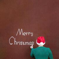 A man writes Merry Christmas with chalk on an abstract surface wearing a Santa hat, Merry Christmas written in chalk on an abstract surface, with space for text photo