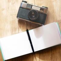 A retro film camera and a notepad with a pen lie on a wooden table, under the rays of the morning sun photo