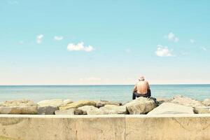 Old man and the sea. An old man sitting on big stone on the seaside. photo