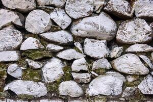 A close-up view of a stone wall composed of irregularly shaped, white stones with patches of moss and dirt. photo