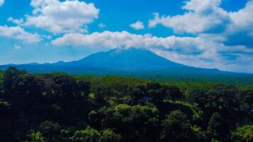 Ranu Bedali Lake in East Java sparkles under a clear blue sky, with Mount Semeru majestically rising in the background. The stunning clouds add to the serene beauty of this breathtaking landscape. photo