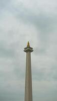 The iconic Monas in Jakarta stands tall against a backdrop of beautiful clouds and lush green grass photo