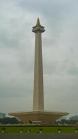 The iconic Monas in Jakarta stands tall against a backdrop of beautiful clouds and lush green grass photo