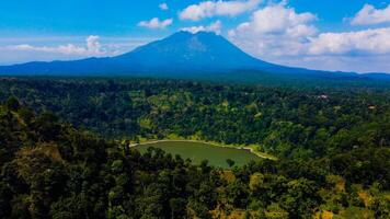 Ranu Bedali Lake in East Java sparkles under a clear blue sky, with Mount Semeru majestically rising in the background. The stunning clouds add to the serene beauty of this breathtaking landscape. photo